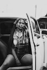 woman in white and black dress shirt and blue denim shorts sitting on car