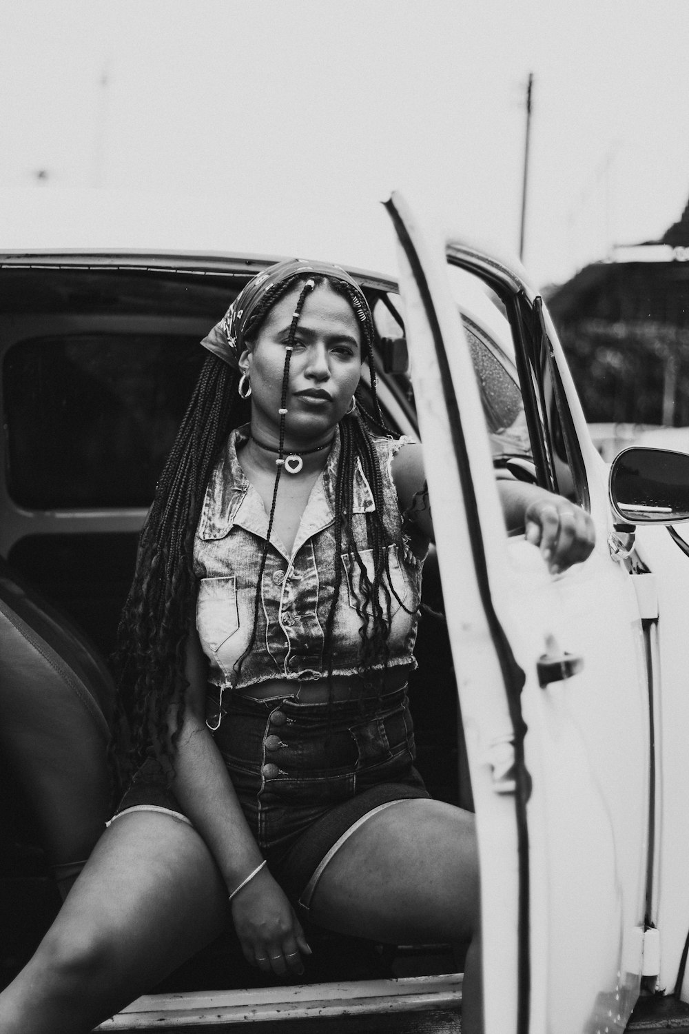 woman in white and black dress shirt and blue denim shorts sitting on car