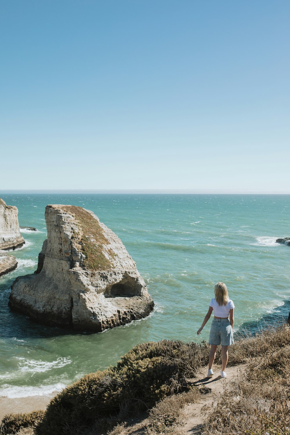 woman in white t-shirt standing on brown rock formation near body of water during daytime