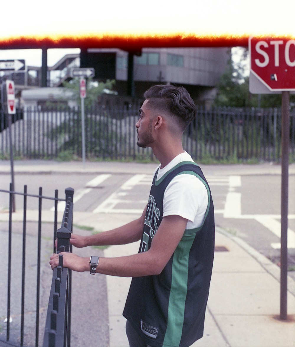 man in green and white polo shirt standing near black metal fence during daytime