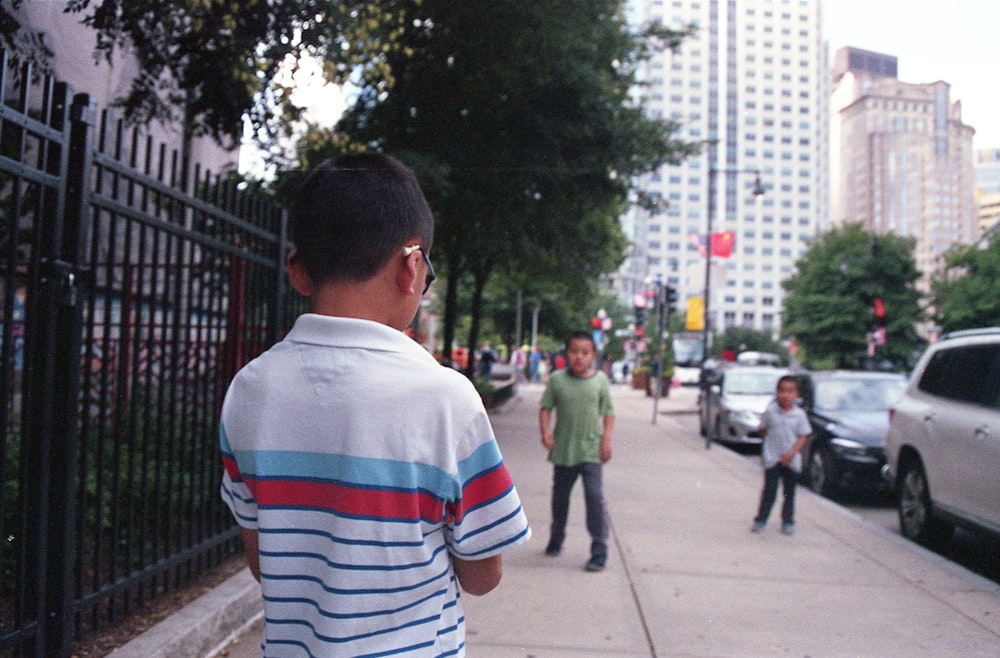 man in white red and blue striped shirt walking on sidewalk during daytime