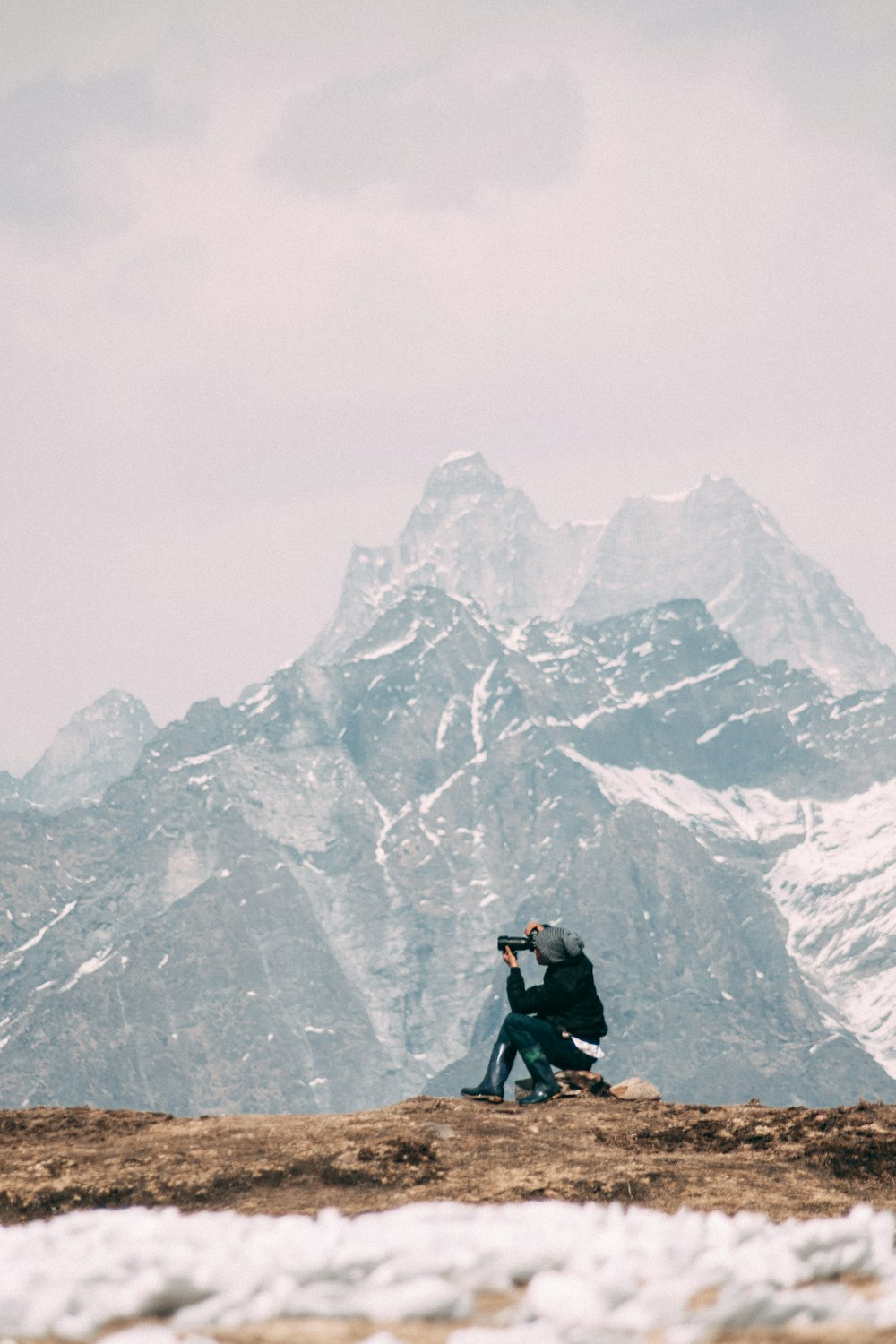 Persona in giacca nera e pantaloni neri che si siede sulla montagna rocciosa durante il giorno