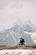 person in black jacket and black pants sitting on rock mountain during daytime