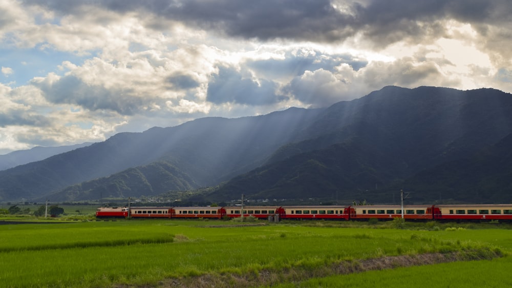 red and white train near green grass field and mountain under white clouds and blue sky