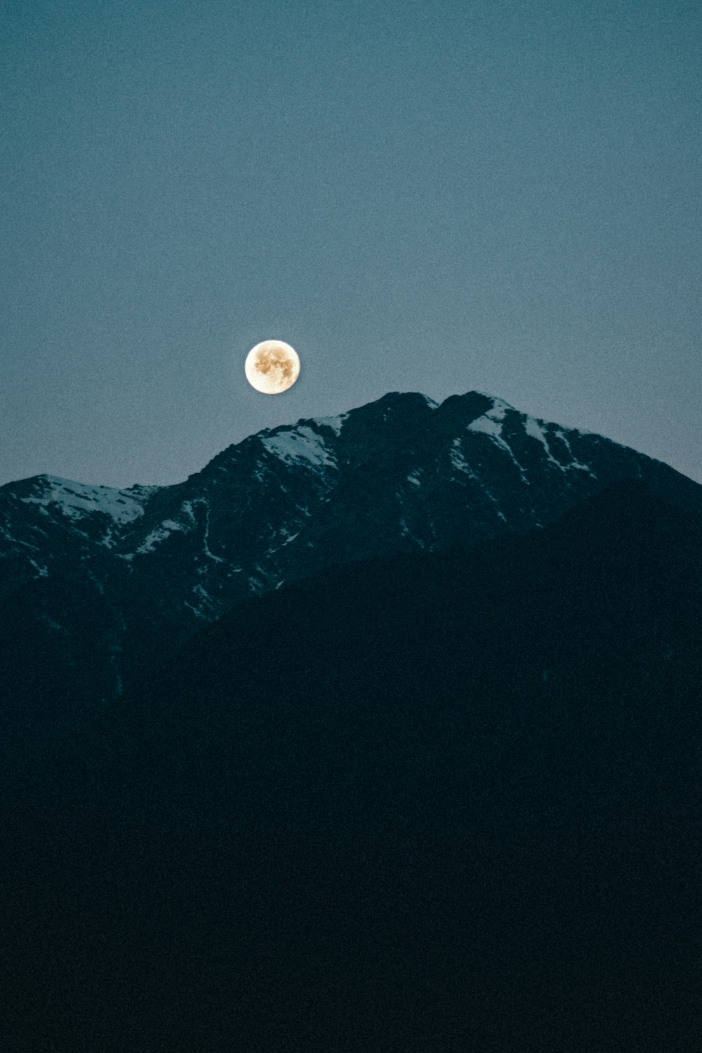 a full moon rising over a mountain range