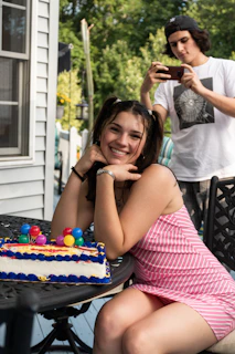 A joyful young woman in an elegant dress smiling during her 15th birthday photo session in a sunlit garden.