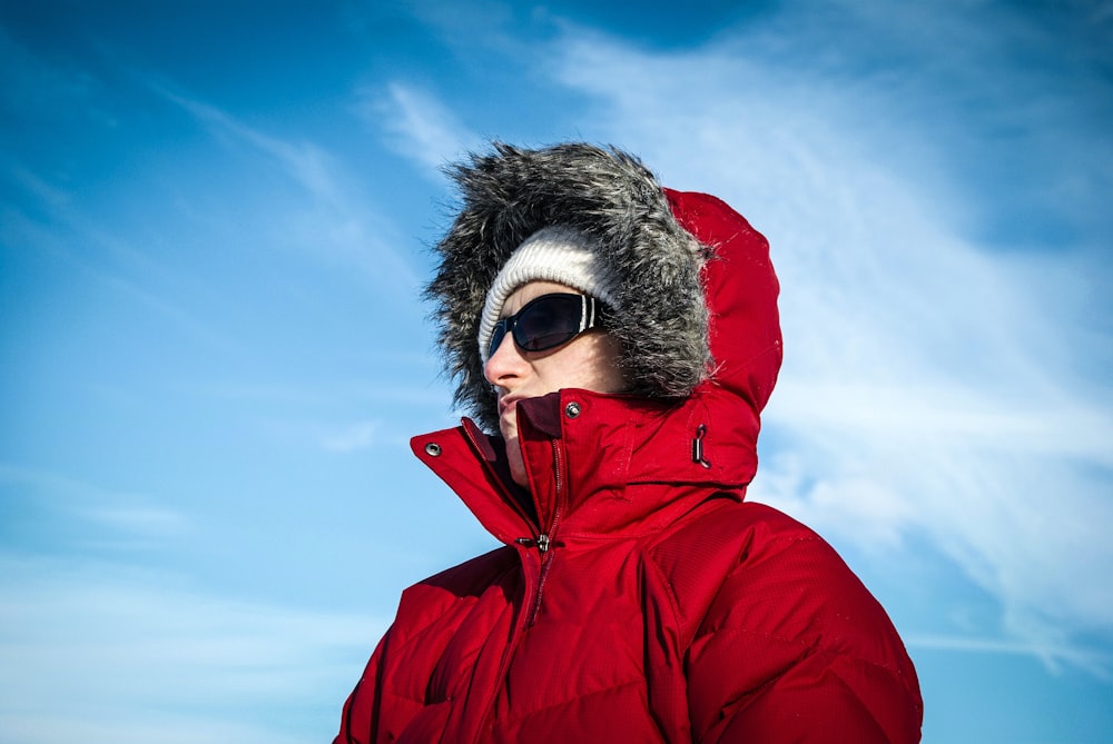 Persona in felpa con cappuccio rossa che indossa occhiali da sole neri sotto il cielo blu durante il giorno