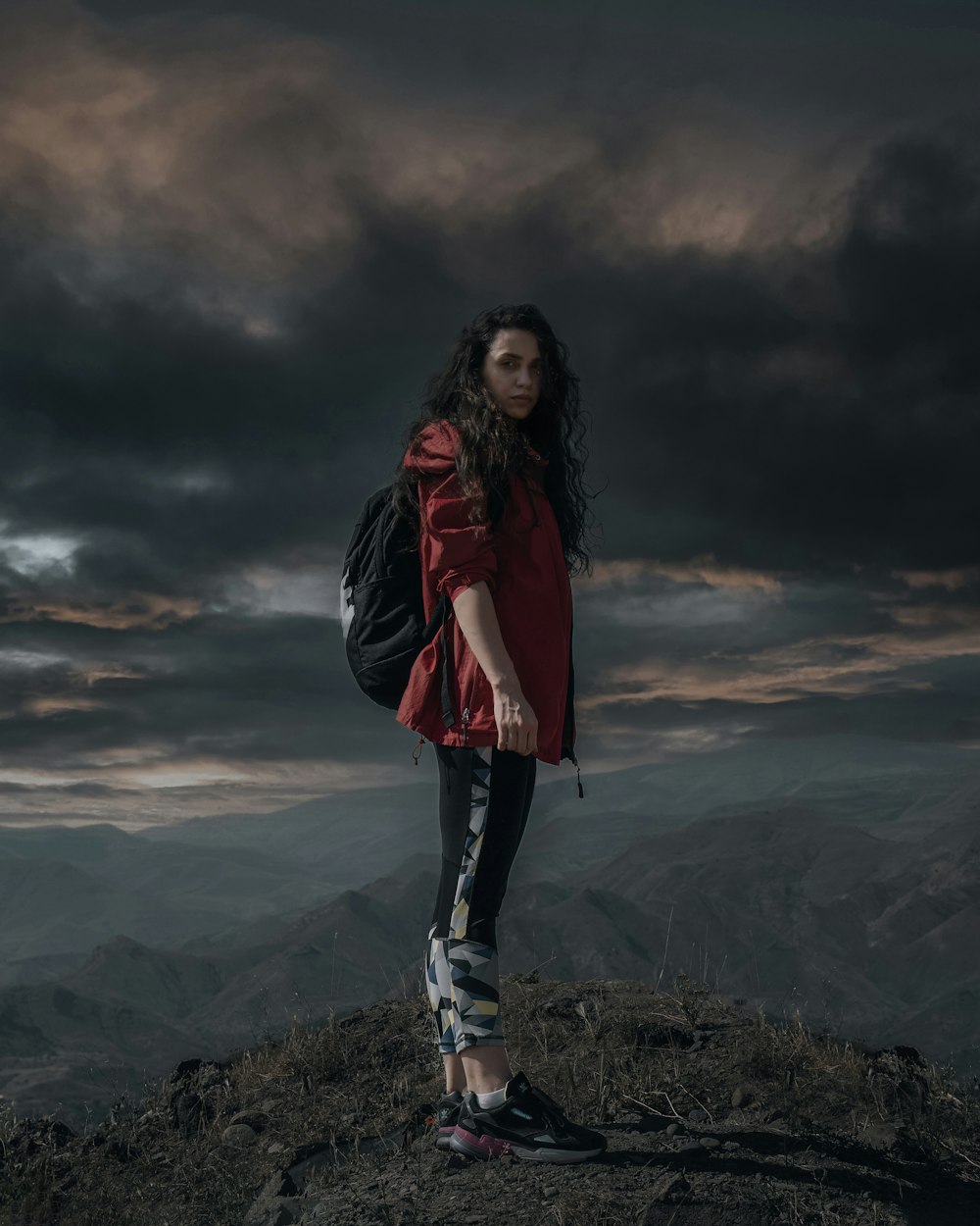 woman in red jacket and blue denim jeans standing on top of mountain during daytime