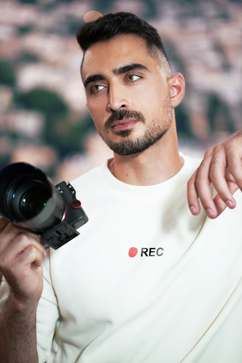Hombre con camiseta blanca de cuello redondo sosteniendo una cámara DSLR negra