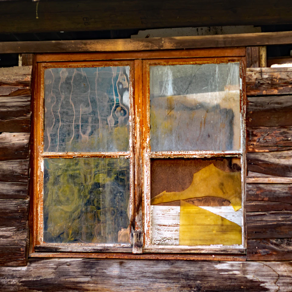 Old, dilapidated wooden window with rusted metal frame and broken panes on a building