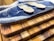 A set of wooden cutting boards stacked on top of each other with unique grain patterns. On the top board, there is a decorative resin wave design in blue and white. Two small wooden sporks are placed on the resin surface.
