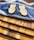 Two wooden sporks are placed on a dark resin cutting board with a wave-like design. The cutting board rests on several stacked wooden boards with varying shades of brown.