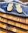 Two wooden sporks are placed on a dark resin cutting board with a wave-like design. The cutting board rests on several stacked wooden boards with varying shades of brown.