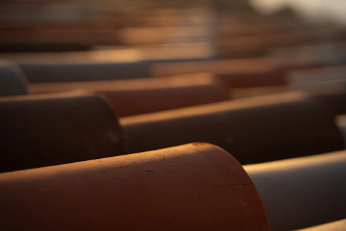 Rows of galvanized iron pipes reflecting light in an industrial storage area.