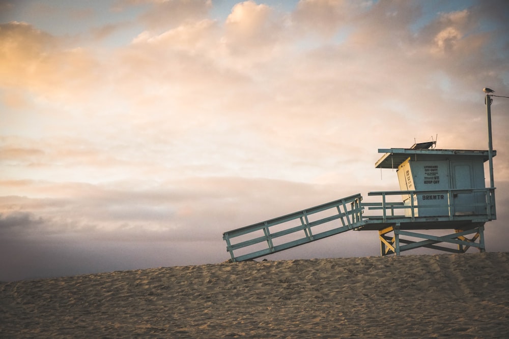 brown wooden lifeguard house on brown sand under white clouds during daytime