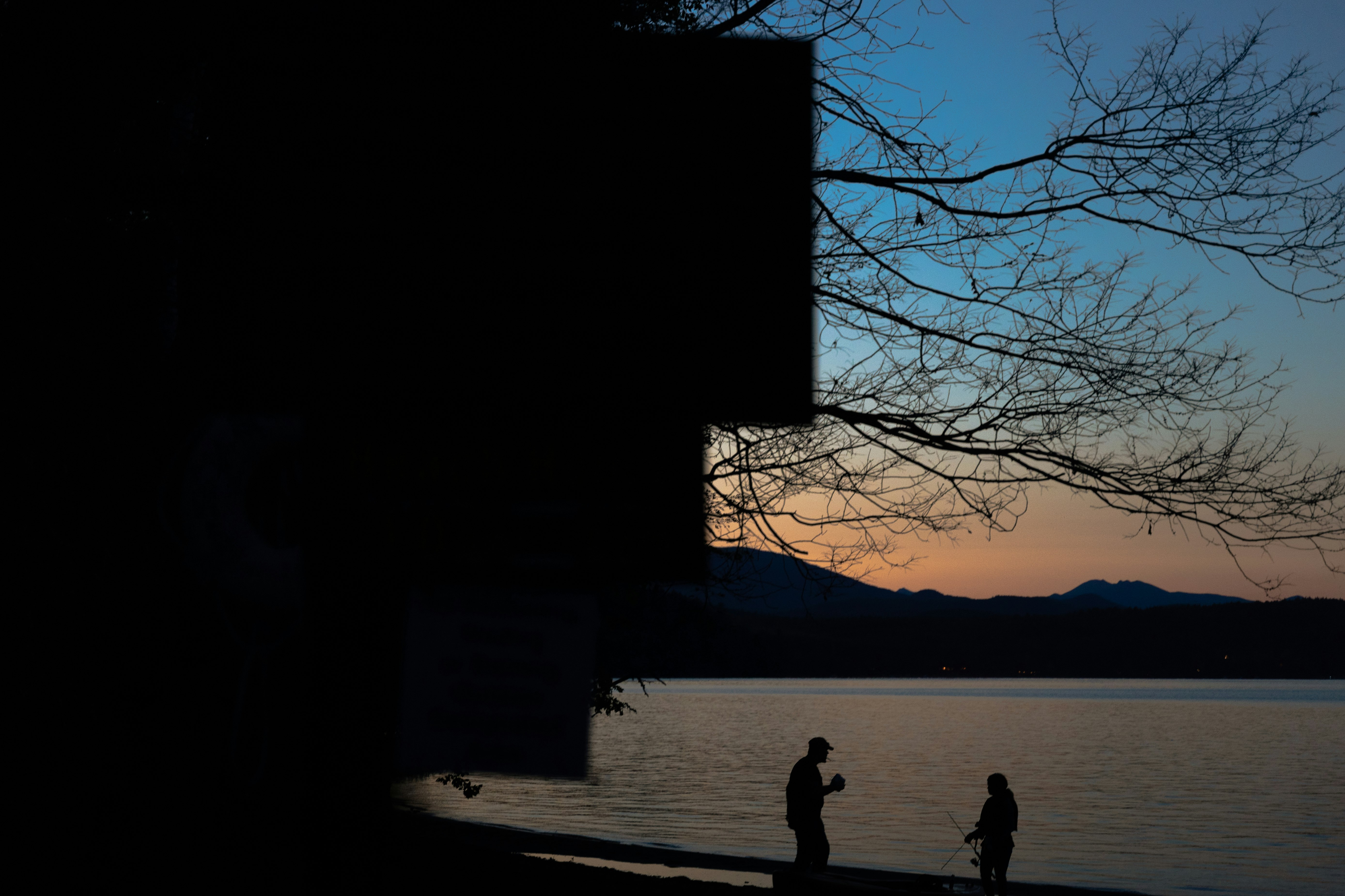 silhouette of person walking on sidewalk near body of water during sunset