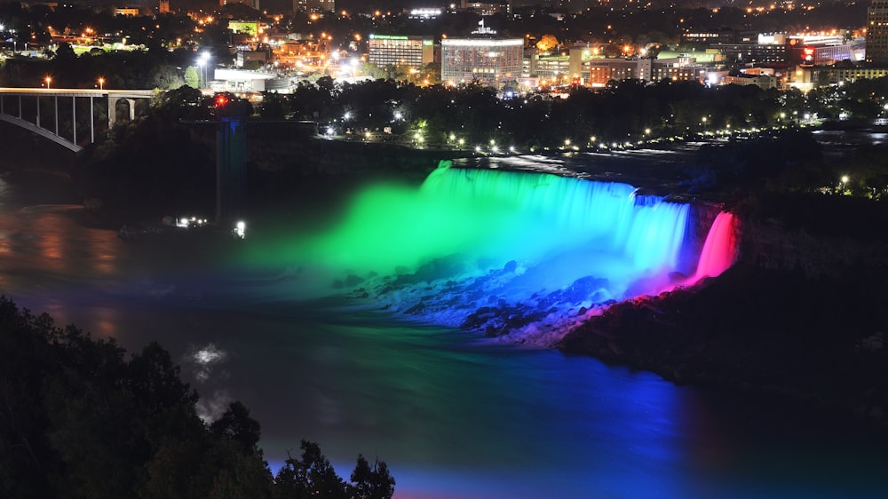 a rainbow colored waterfall in a city at night
