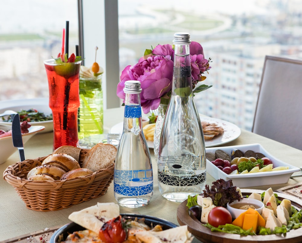 clear glass bottle beside brown woven basket with fruits on table