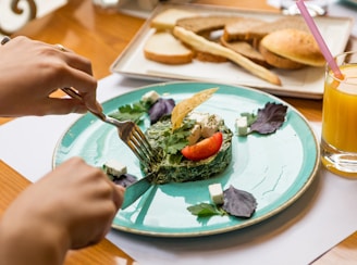 person holding fork and knife slicing vegetable on white ceramic plate