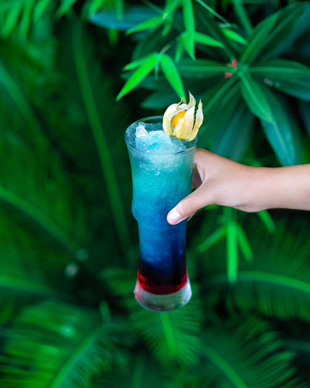 person holding clear drinking glass with blue liquid