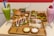 A variety of dishes are laid out on wooden platters, featuring a burger with lettuce and tomato, a hot dog drizzled with mayonnaise, a wrap with mixed fillings, and an assortment of dips and side salads. There are two vibrant smoothies, one green with a kiwi slice and another pink with a strawberry on top. Fried falafel balls and fresh sliced vegetables are also present, creating a colorful and appetizing display.