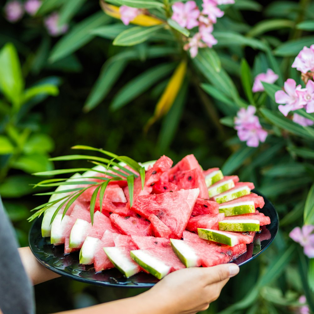 person holding a black round plate with sliced watermelon