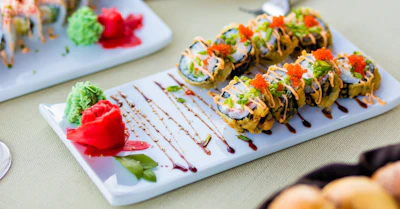 Elegant plating of sushi rolls with colorful sauces and edible flowers.