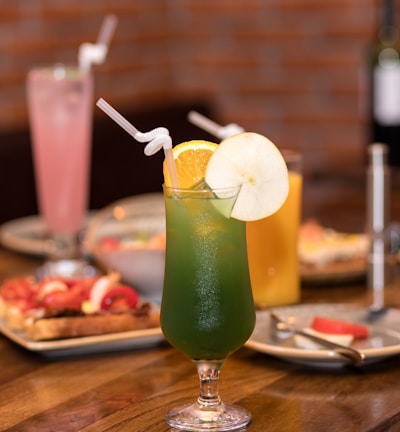 clear drinking glass with green liquid and sliced lemon on brown wooden table