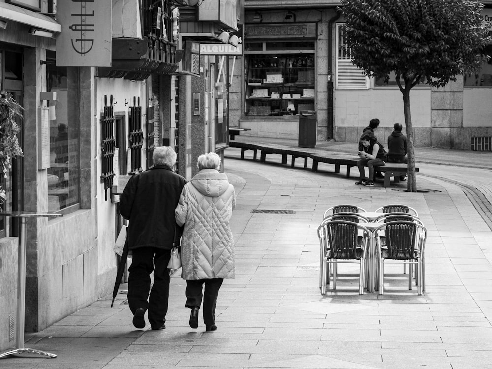 grayscale photo of woman in coat walking on sidewalk