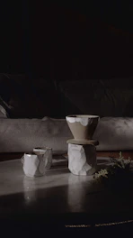 A cozy studio scene with bright, hand-thrown stoneware cups and bowls arranged on a wooden table bathed in natural light.