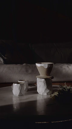 A cozy arrangement of terracotta mugs and cream-colored bowls on a rustic wooden table bathed in soft natural light.