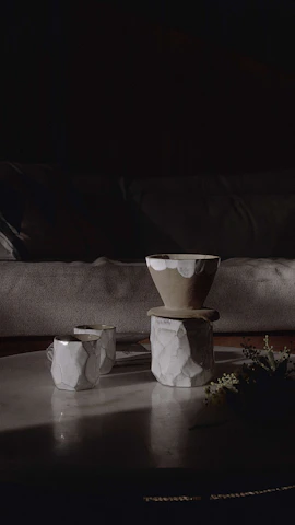 A cozy studio scene with bright, hand-thrown stoneware cups and bowls arranged on a wooden table bathed in natural light.