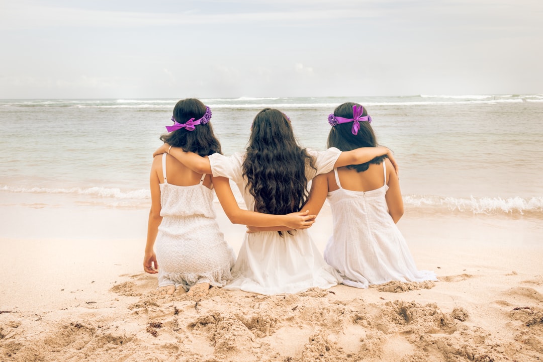 2 women in white dress sitting on white sand beach during daytime