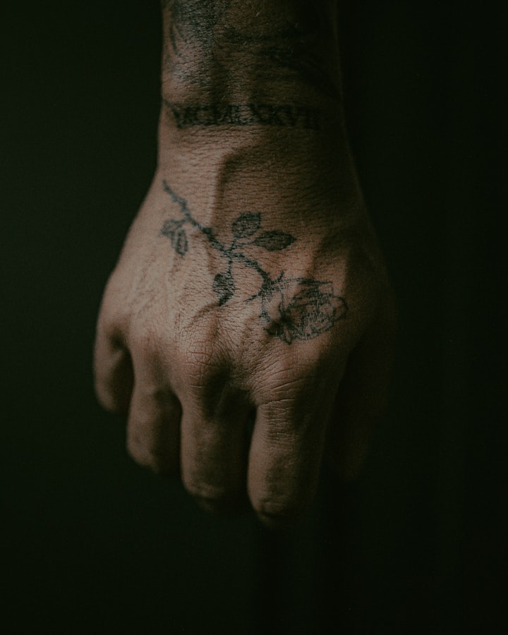 A black-and-red floral tattoo on a person's hand, the red ink echoing the red crosshair center of flash design №002