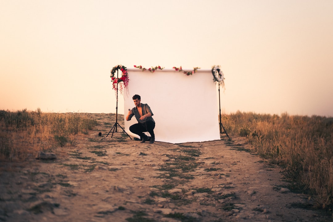 man in black shirt and black pants sitting on rock near body of water during daytime