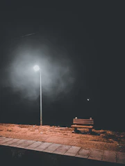 An empty bench under a flickering street lamp at dusk, evoking solitude.