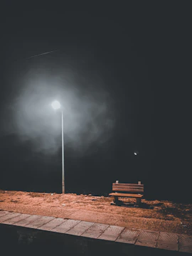 An empty bench under a flickering street lamp at dusk, evoking solitude.