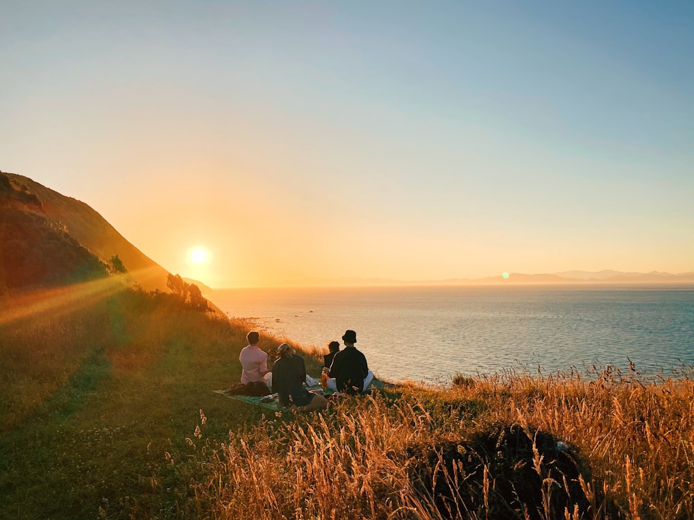 2 person sitting on green grass field near body of water during sunset