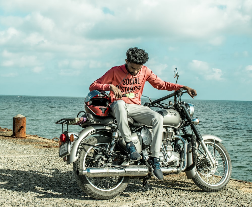 man in red shirt riding on black motorcycle near sea during daytime