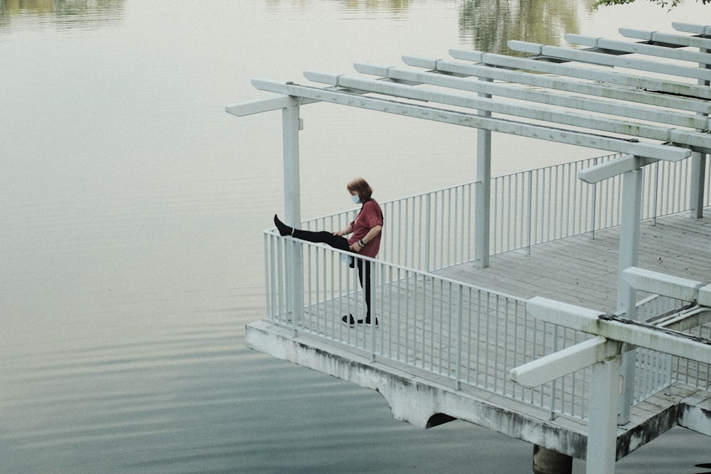 man in red shirt and black pants sitting on white wooden fence