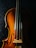 A close-up view of a wooden string instrument, focusing on the body and strings. The warm, natural wood tones contrast with the dark background, highlighting the instrument's curves and craftsmanship.