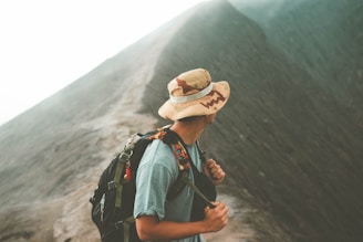 man in brown hat and blue denim jacket standing on mountain during daytime