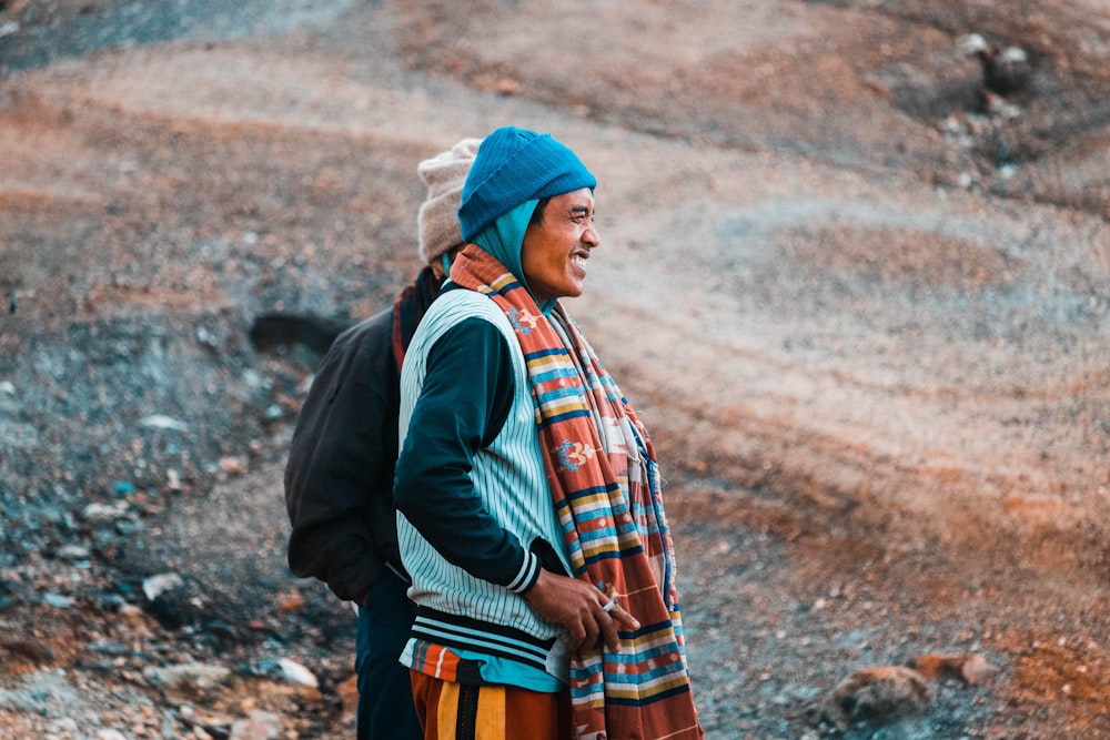 man in black jacket and orange and white plaid scarf standing on rocky ground during daytime