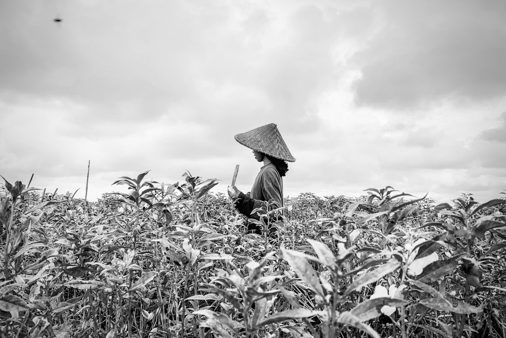 grayscale photo of person wearing hat in the middle of plants