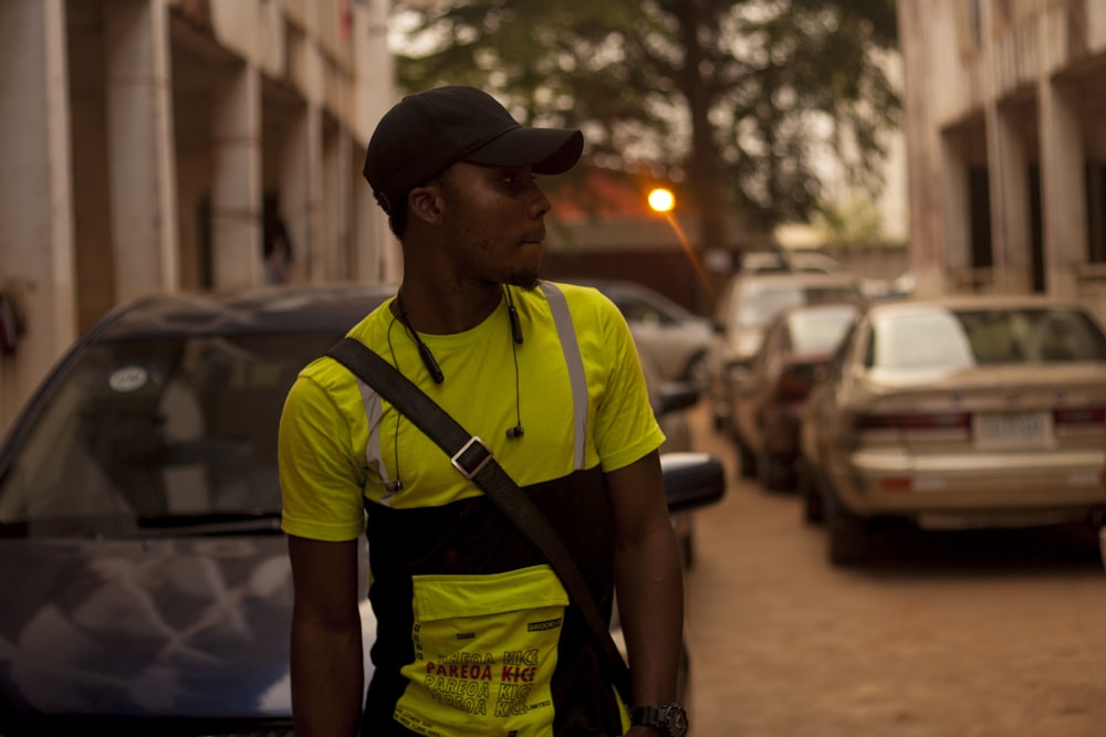 man in green t-shirt and black cap standing on sidewalk during daytime