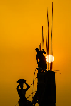 A friendly construction worker holding blueprints in front of a building site at sunset.