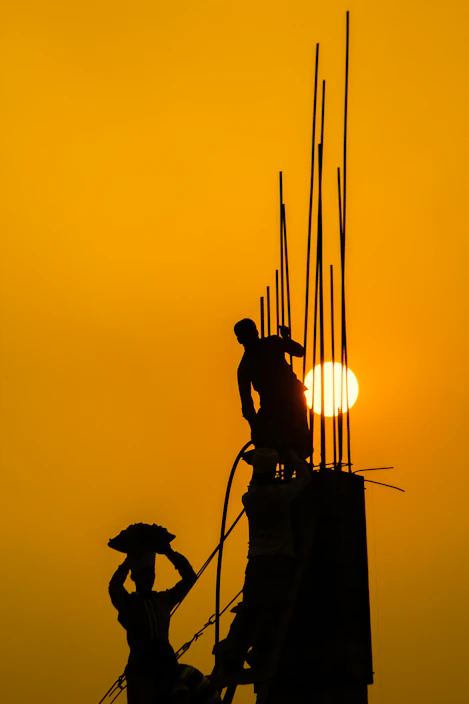 Construction site showing workers handling TMT steel bars under bright sunlight.