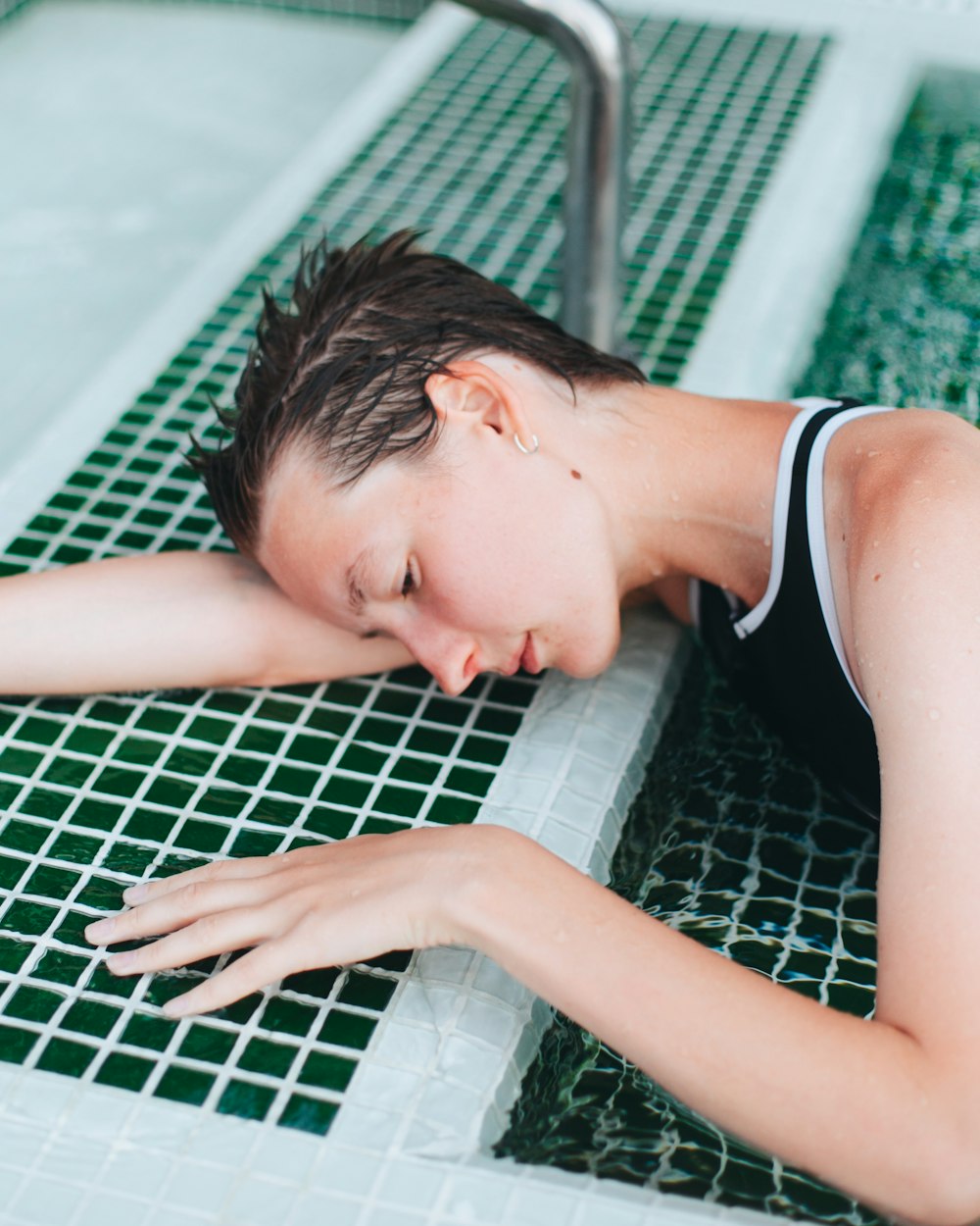 woman in black tank top lying on green and white ceramic tiles