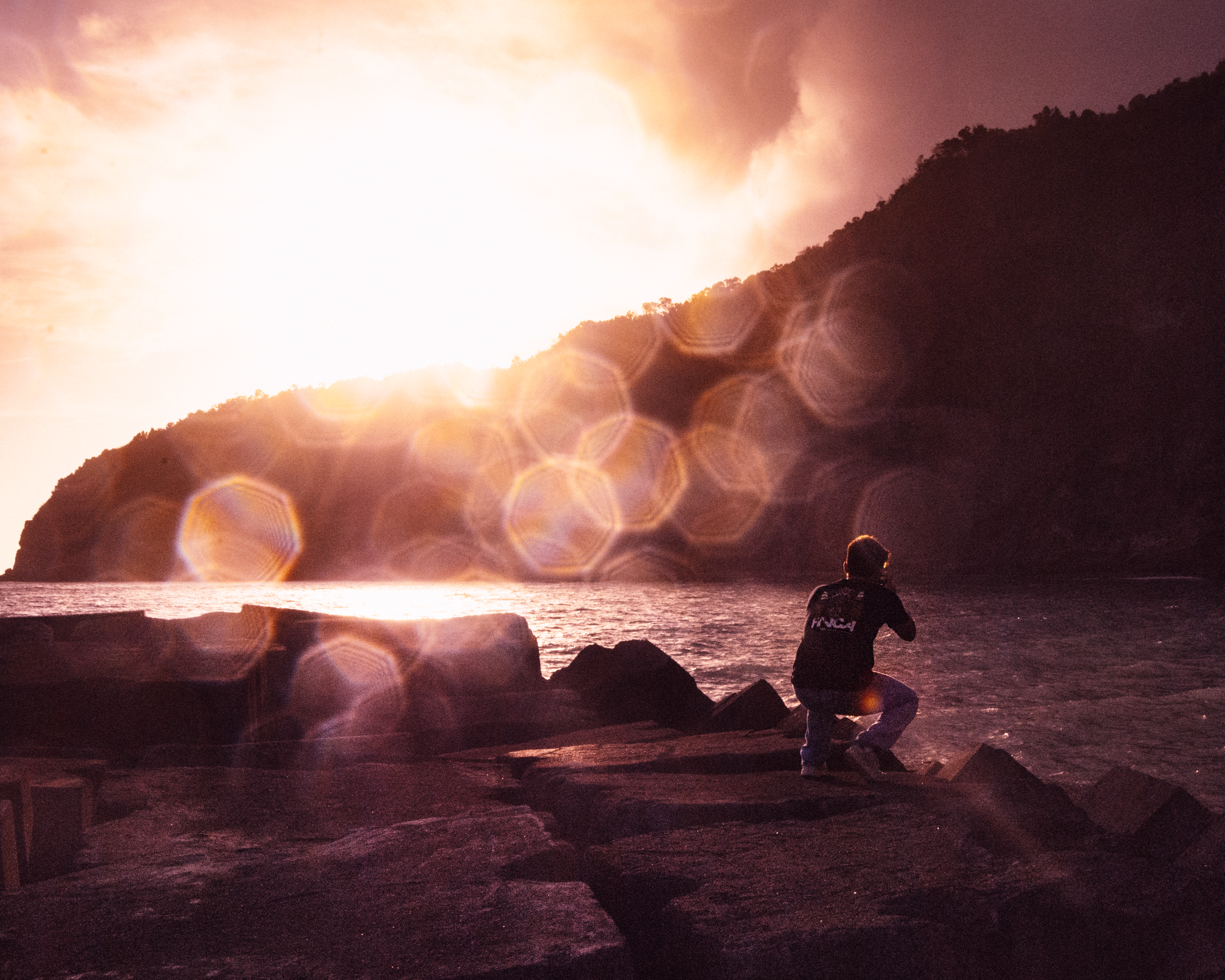 homem sentado na rocha perto do corpo de água durante o pôr do sol