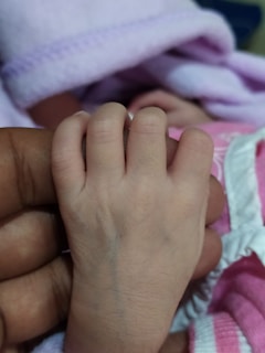 Close-up of tiny baby hands holding Bruna’s finger against a soft pink quartz background.